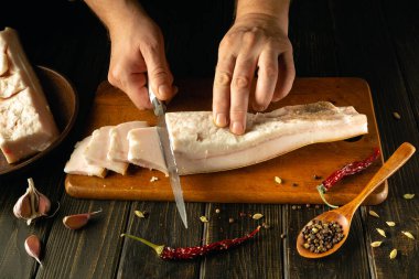 Eller, ahşap bir kesme tahtasındaki kalın domuz göbeğini ustalıkla kesiyor. Ukrayna ulusal yiyeceği.