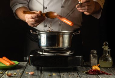 Sıcak bir mutfakta, şef kaynayan bir tencereye taze sosis ve karabiber ekleyip lezzetli bir yemek yapar. Ilık ışık, zengin aromalarla dolu mutfak atmosferini güçlendiriyor..