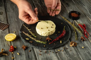 Eller, kremsi peynir tekerinin etrafına taze otlar ve baharatlar dizer. Kırsal ahşap masa davetkar atmosferi arttırır. Mutfak yapımı ya da toplanması için mükemmeldir..