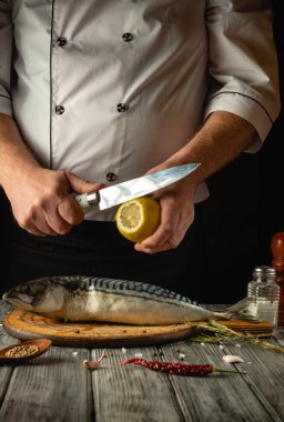 Yetenekli bir şef ahşap kesme tahtasındaki taze balığı hazırlarken ustalıkla bir limonu dilimler. Baharat ve şifalı bitkiler, mutfak deneyimini geliştirmek,.