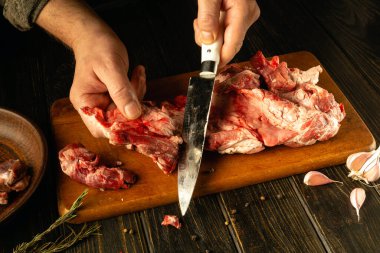 Yetenekli bir el ahşap kesme tahtasına ustalıkla taze et oyar. Yaklaşan bir tabakta sarımsak ipuçları gibi etrafını saran malzemeler sıcak bir mutfak atmosferi yaratıyor..