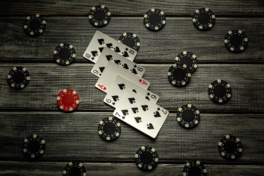 Heyecan verici bir poker oyunu, yüksek kart kombinasyonu ve çeşitli poker çiplerinin yer aldığı rustik ahşap bir masada sergileniyor ve oyuncular için gergin bir atmosfer yaratıyor..