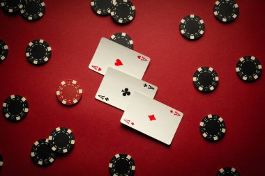 Poker fişleri ile çevrili kırmızı bir masanın üzerine üç farklı kombinasyonu olan birkaç iskambil kağıdı. Poker kulübünde atmosfer beklenti ve stratejiyle doludur..