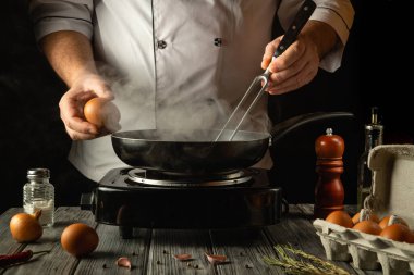 Bir şef taze yumurtaları sıcak tavaya kırarak lezzetli bir yemek yapmaya hazırlanır. Buhar, aşçılık büyüsü bir saat erken saatte başlar ve yanında sofrada kırsal malzemeler vardır..