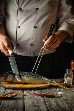 Yetenekli bir şef, keskin bir bıçakla taze bir balığı çatalla doğruyor. Şefin odaklanmış tavrı, mutfaktaki mutfak sanatının hassasiyetini vurguluyor..