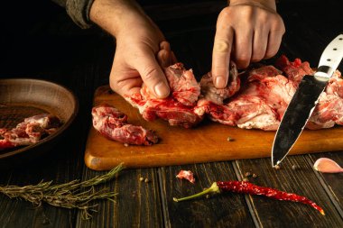 Eller ahşap bir tahtanın üzerinde, aromatik otlar ve baharatlarla çevrili taze et kesimlerini ustalıkla hazırlar. Mutfağın sıcak renkleri mutfak yaratıcılığı için davetkar bir atmosfer yaratıyor..