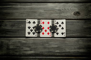 Gri bir masa ve çipin üzerinde üç yedinin galibiyet kombinasyonuyla kağıt oynamak. Pokerde kazanmak servete bağlıdır..