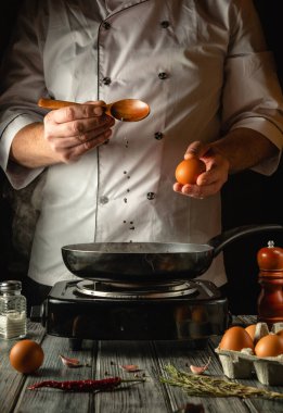 Tecrübeli bir şef sıcak tavaya kaşıkla karabiber ekler. Bu mutfağın sıcak atmosferi yemek yapma sevgisi ve lezzetli yemekler yaratma sevincini vurguluyor..