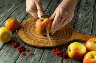 Eller, sulu narenciye meyveleri ve taze böğürtlenlerle çevrili taşralı ahşap bir tahtanın üzerinde ustalıkla canlı bir elma kesiyor. Sıcak renkler mutfak ortamında davetkar bir atmosfer yaratıyor..