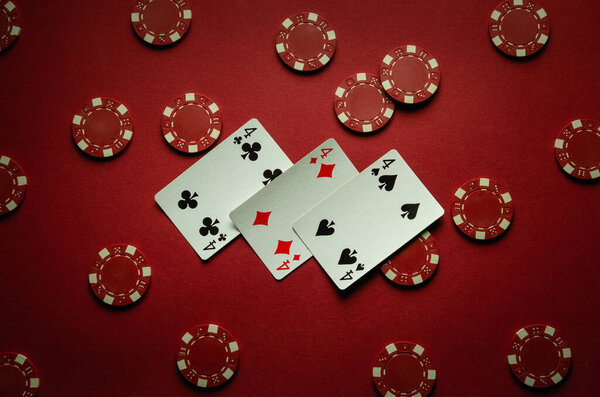 On the red table in the club there are chips and playing cards with a successful combination of three of a kind or set. The concept of a good win in the game of poker.