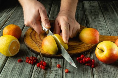 Elleri, canlı meyvelerle çevrili, olgun bir elmayı, kırsal bir tahta üzerinde ustalıkla dilimliyor. Limon ve böğürtlenin parlak renkleri iştah açıcı görüntüyü güzelleştiriyor ve sağlıklı bir ziyafet çekiyor..