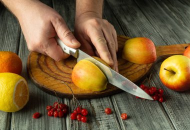 Eller, canlı narenciye meyveleriyle çevrili taşralı ahşap bir tahtanın üzerinde ustalıkla olgun elmaları kesiyor. Atmosfer sıcak ve davetkar. Mutfak macerası için mükemmel..