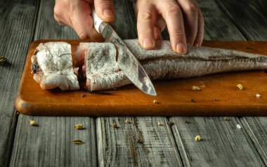 Sıcak bir mutfak ortamında, elleri ustalıkla kesilmiş ahşap bir tahtanın üzerinde taze bir balık filetosu yapıyor. Hazırlığın büyüleyici ayrıntıları, baharatlarla çevrili mutfak becerilerinin sanatını vurguluyor..