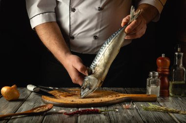 Yetenekli bir şef, yeni yakalanmış bir balığı tahta kesme tahtasında sunar. Sahneyi saran soğan ve baharat gibi malzemeler aşçılık sanatını ön plana çıkarıyor..