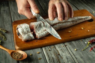 Becerikli bir aşçı, çeşitli otlar ve baharatlarla çevrili, sade ahşap bir kesme tahtasının üzerinde yeni yakalanmış bir balığı dilimliyor..