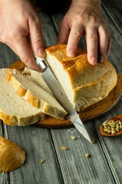 Bir çift el, altın bir somun ekmeği keskin bir bıçakla ustalıkla keser. Sıcak, taze koku havayı doldurur. Kabuklu dış görünüşü yumuşak bir iç mekanı ortaya çıkarır. Paylaşmak için mükemmeldir..