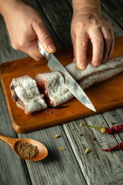 Eller, sıcacık bir mutfak ortamında baharat ve aletlerle çevrili iyi giyimli ahşap bir tahtanın üzerinde ustalıkla taze bir balığı dilimler. Sıcak melodiler yemek pişirmek için davetkar bir ortam yaratıyor..