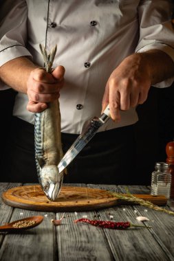 Kendini adamış bir şef, bir balığı ahşap bir kesme tahtasında hazırlarken ustalıkla tutar. Mutfak, baharat ve otlarla dolu ve mutfak işçiliği atmosferine ekleniyor..