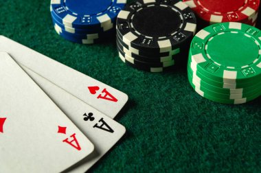 Etrafı renkli poker fişleri ile çevrili yeşil bir keçeli masa üzerinde üç as yatıyor. Oyuncular eğlenceli bir akşamda bir sonraki hamlelerini yaparken atmosfer geriliyor..