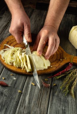 Ahşap kesme tahtasının üzerinde marifetli bir şekilde lahana dilimler. Çevreleyen malzemeler arasında taze otlar, sarımsak ve kurutulmuş kırmızı biberler var..