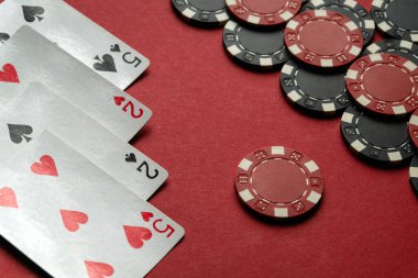 Bir çift ikiliyi ve bir çift beşliği gösteren dört iskambil kağıdı parlak kırmızı bir masadaki kırmızı ve siyah çiplerin yanında uzanarak poker aşıkları için davetkar bir ortam yaratıyor..