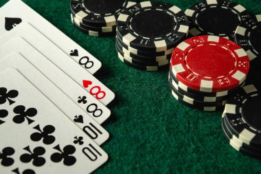 Yakın plan çekimde, yeşil bir keçeli masa üzerindeki çeşitli poker çiplerinin yanında full house ya da full boat 'u gösteren bir iskambil kağıdı serisi var. Oyunun heyecanı aşikar..