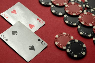 İki çift iskambil kağıdını gösteren iki kart dağınık poker çiplerinin yanında kırmızı bir keçeli masa üzerinde dinleniyor, kart oyuncuları için çekici bir atmosfer yaratıyor..