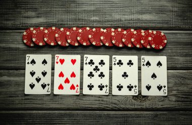 Kırmızı poker fişleri ile birlikte kalpler ve kulüplerin yer aldığı bir iskambil kağıdı kırsal bir ahşap yüzeye serilir ve arkadaşlar arasında oyun gecesi için samimi bir ortam yaratır..