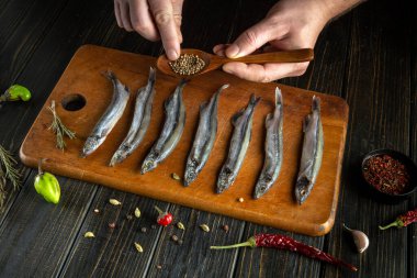 Aşçının elleriyle kesme tahtasının üzerinde kapelinli balık pişirmek. Tadı ve aroması için balığa ahşap kaşıkla kişniş ekliyorum. Balık diyeti kavramı.