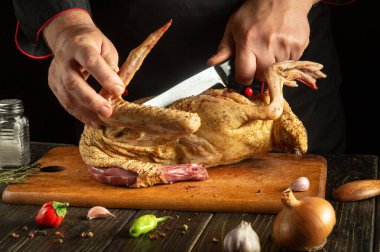 Yetenekli bir şef, tahta kesme tahtasındaki kümes hayvanlarını kesmek için keskin bir bıçak kullanır. Taze otlar, sarımsak ve biberler tüm bölgeyi sarmış, canlı bir aşçılık ortamı sergiliyorlar..