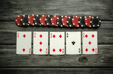 Renkli bir iskambil kâğıdı seti 2 ila 5 karo ası ve kırsal bir masanın üzerinde kırmızı ve siyah poker fişleri ile çevrili bir sinek ası oyun gecesi için mükemmel..