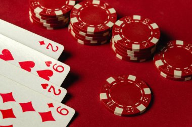 İkili ve dokuzluları gösteren dört oyun kartının yanına istiflenmiş kırmızı poker fişleri. Parlak renkler, kumarhanelerde sıklıkla rastlanan canlı atmosferi vurgular.