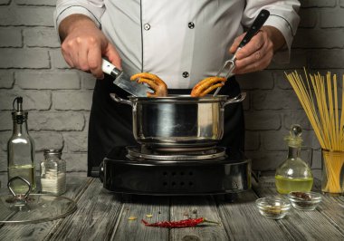 Kırsal dokunuşları olan modern bir mutfakta, bir şef fırında makarna pişirirken ustalıkla tavuk ayağını hazırlar, mutfak becerisi ve konsantrasyonunu gösterir..