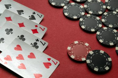 Kâğıt oyunlarının kazanan kombinasyonu dört farklı kart ve siyah poker çipleri kırmızı keçeli masa boyunca dağılmış durumda. Atmosfer sıradan ve stratejik bir oyun gecesi olduğunu gösteriyor..