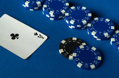 Mavi poker masasında, stratejik olarak poker fişleri istiflenmiş bir sinek ası var. Atmosfer canlı ve heyecan havayı dolduruyor..