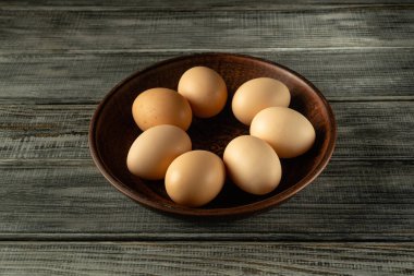 Değişik şekil ve gölgelerden oluşan taze yumurtalar, dokulu ahşap bir yüzey üzerinde duran ve doğal ve organik bir his uyandıran koyu bir ahşap kaseye güzelce yerleştirilir..