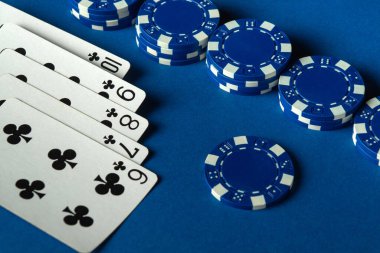 Kazanan floşu gösteren kartlar parlak mavi bir yüzey üzerinde poker fişleri ile eşleştiriliyor. Bu da kumarhane ortamında canlı bir oyun oynandığını gösteriyor..
