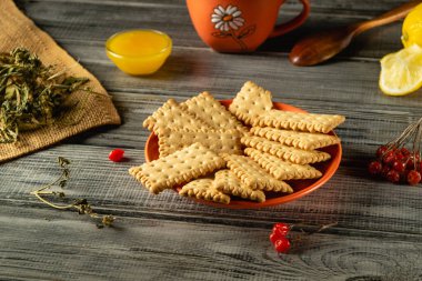 Canlı bir portakal tabağında taze otlar, limon dilimleri, bir fincan şeker ve küçük bir kase tatlı sosla çevrili gevrek krakerler bulunur..