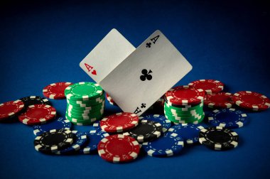 Çok sayıda renkli poker fişi ile çevrili iki as kart oyunu sergileniyor. Sahne parlak mavi bir arkaplana göre ayarlanmış, oynamak için mükemmel enerjik bir atmosfer yaratıyor..
