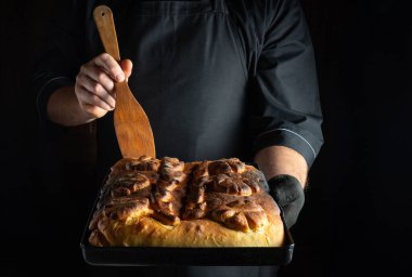 Siyah önlük takan bir aşçı, elinde karmaşık tasarımları olan bir tepsi taze ekmek tutar..
