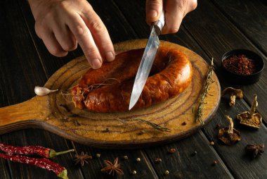 Kırsal ahşap bir kesme tahtasına lezzetli bir sosis dilimler. Yemek pişirme deneyimini geliştirmek için çeşitli otlar ve baharatlar kullanılıyor..