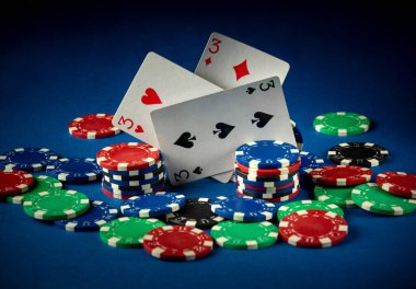 Birçok renkli poker fişi ile çevrili üç iskambil kartı kaotik bir şekilde gösterilir. Sahne parlak mavi bir arkaplan üzerine kurulmuş, heyecan verici bir atmosfer yaratıyor. Oynamak için mükemmel..