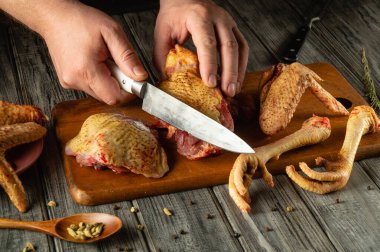 Mutfak aletleri ve taze malzemelerle çevrili ahşap bir tahtanın üzerinde tavuk parçalarını ustalıkla kesiyorlar..
