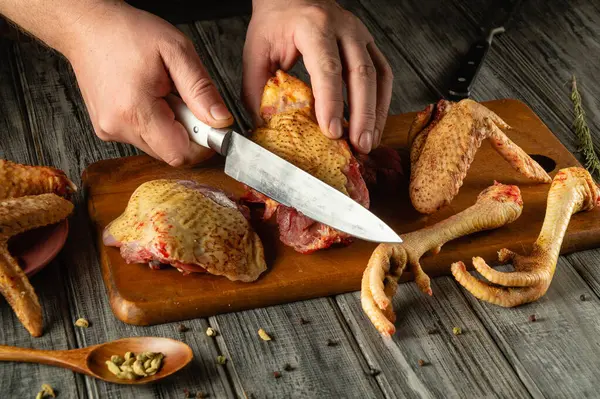 Mutfak aletleri ve taze malzemelerle çevrili ahşap bir tahtanın üzerinde tavuk parçalarını ustalıkla kesiyorlar..