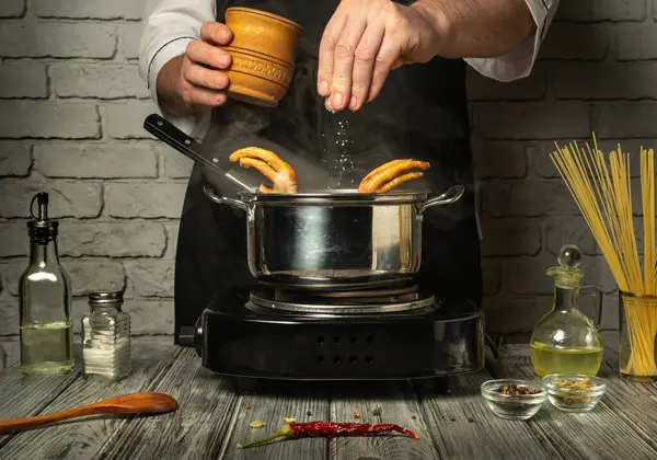 Bir şef tavuk ayağını ocakta tuzla mevsim eder ve lezzetli bir yemek yapar. Taze malzemeler tencerenin etrafına dizilir ve modern mutfak ortamında çorba yapma sürecini geliştirir..