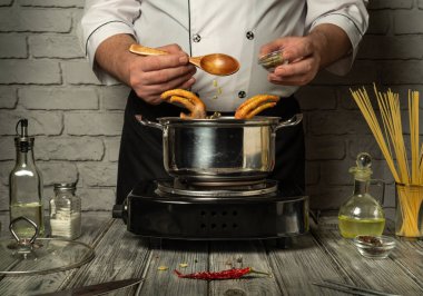 Becerikli bir şef, çeşitli mutfak aletleriyle çevrili bir tencereye özenle baharat ve malzeme koyar ve çağdaş bir ortamda lezzetli bir yemek yaratır..