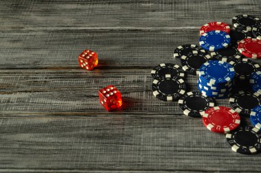 Çeşitli renklerde poker çipleri, kırsal ahşap bir yüzeyde iki kırmızı zarın yanında, gündelik masa üstü oyunları için canlı ve davetkar bir atmosfer yaratıyor..