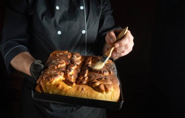 Elinde taze pişmiş ekmek tepsisi tutan bir fırıncı, jöleli, loş bir mutfakta duruyor. Sanatçının detaylara odaklanması, kendini pişirmeye adadığını gösteriyor..