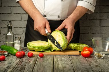 Bir şef ahşap kesim tahtasıyla lahana keser. Etrafı taze domatesler, salatalıklar ve turplarla çevrilidir..