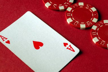 Kırmızı bir masa, birkaç kırmızı poker fişi ile birlikte bir Kupa Ası 'nın yer aldığı bir oyun kartı sergiliyor. Heyecan verici bir kart oyunu gecesi için ortam hazırlıyor..
